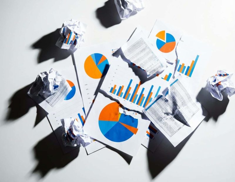 verspreide data visualisaties met kleurrijke grafieken en verfrommelde spreadsheets op witte ondergrond met dramatische belichting