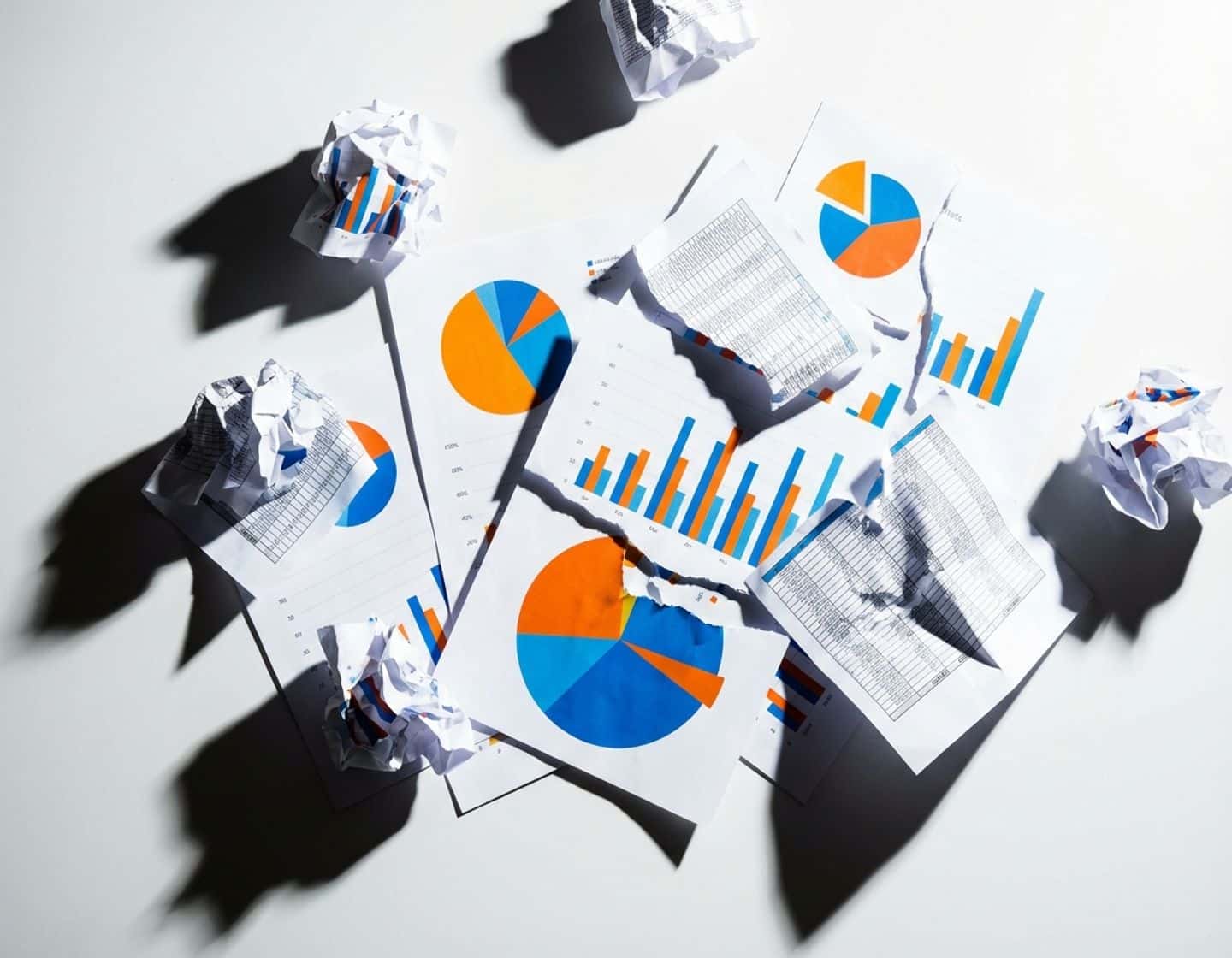 verspreide data visualisaties met kleurrijke grafieken en verfrommelde spreadsheets op witte ondergrond met dramatische belichting