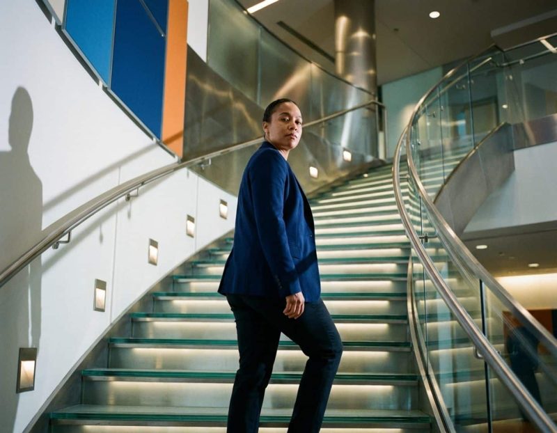 zelfverzekerde ingenieur in marineblauw jasje loopt moderne glazen trap op in strak bedrijfsgebouw