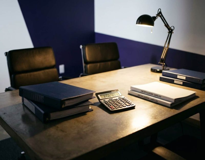 moderne kantoorbureau met rekenmachine met financiële cijfers, lege stoelen en sollicitatieformulieren onder bureaulamp