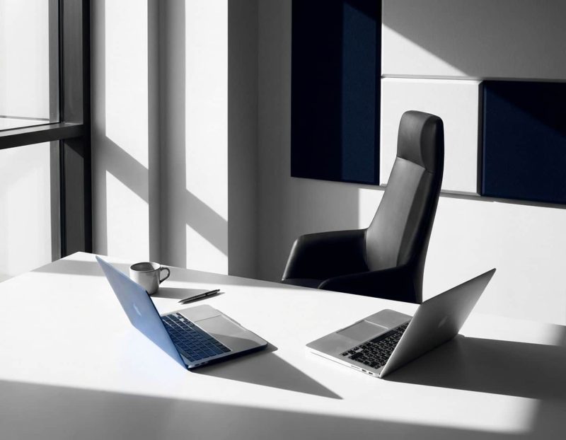 moderne kantoorwerkplek met open laptop en lege stoel, dramatische belichting creëert sterke schaduwen op wit bureau