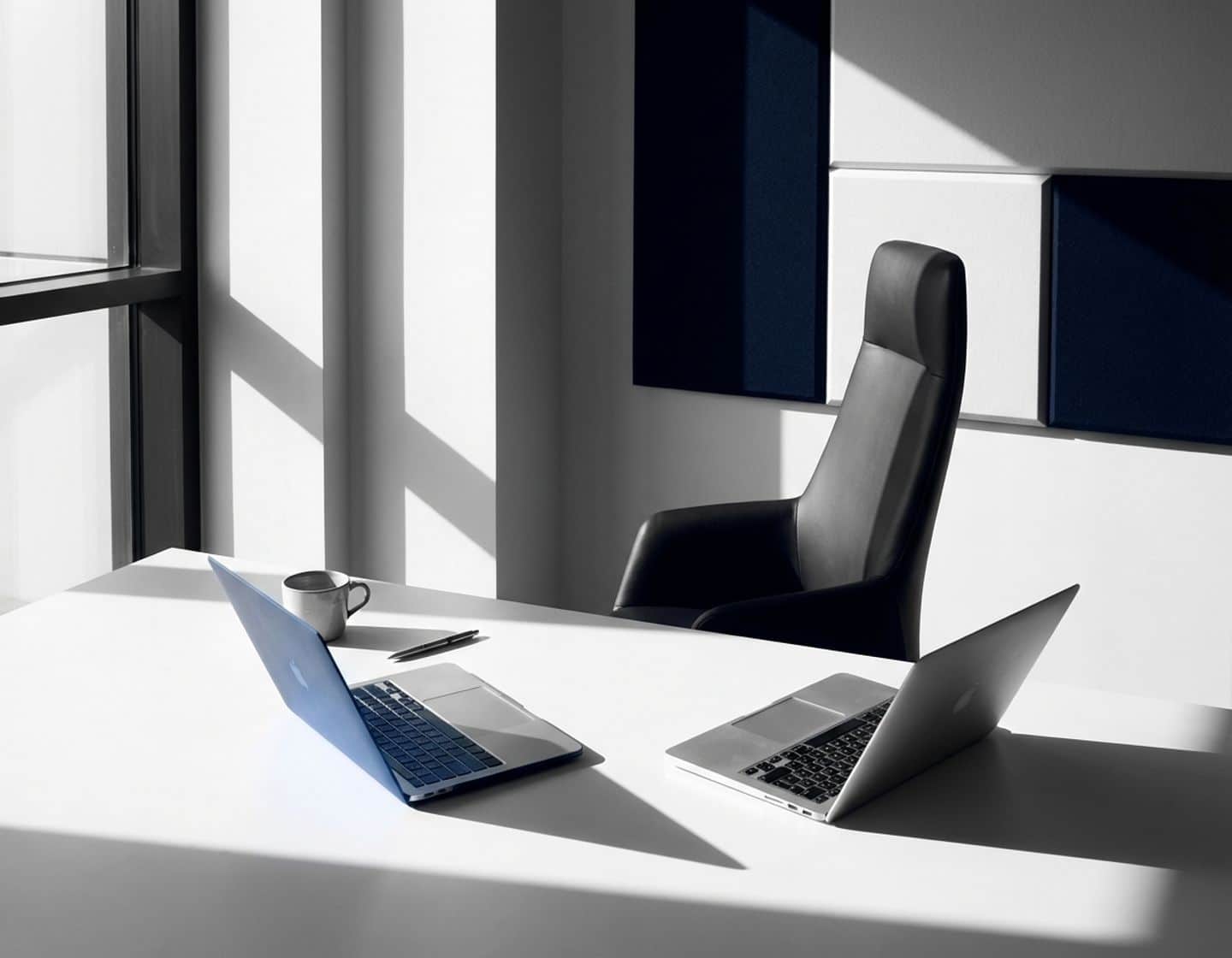 moderne kantoorwerkplek met open laptop en lege stoel, dramatische belichting creëert sterke schaduwen op wit bureau