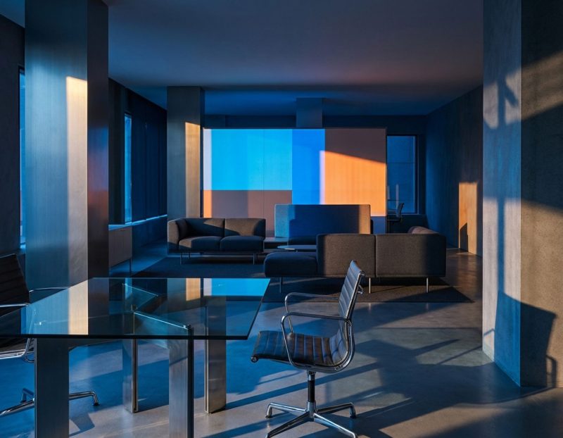 moderne kantooromgeving met glazen vergadertafel, minimalistische werkplek en dramatische blauwe en oranje verlichting