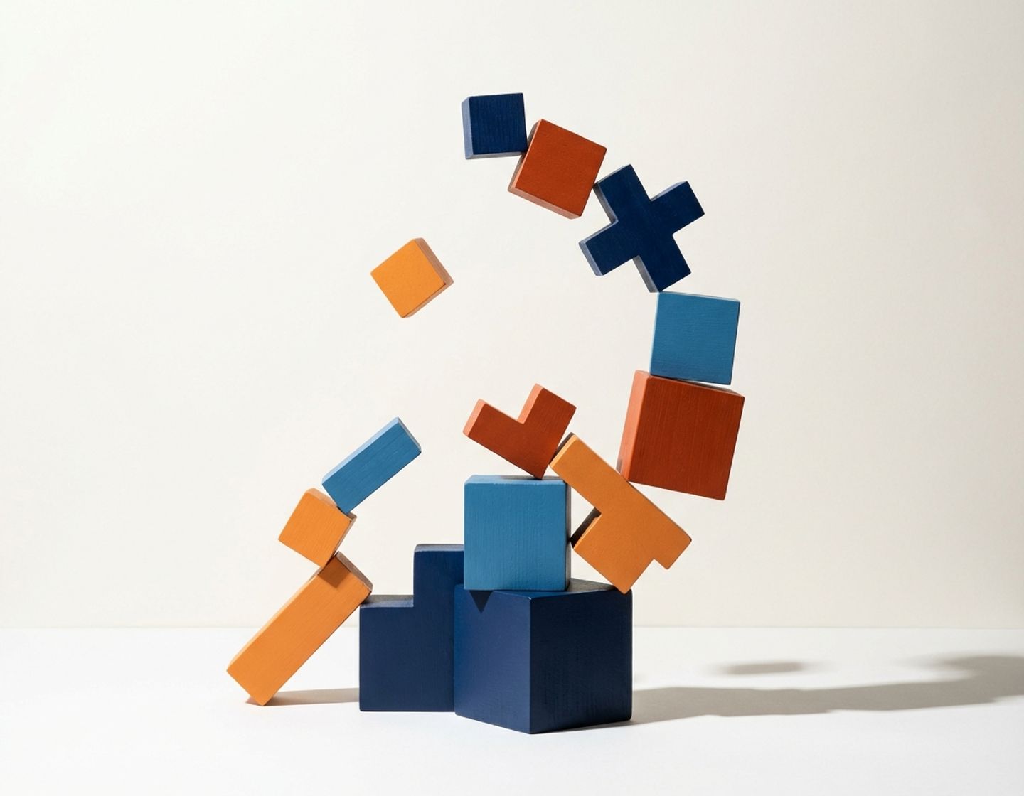 geometrische bouwblokken in blauw en oranje gestapeld in oplopende formatie, sommige vallen weg op witte achtergrond