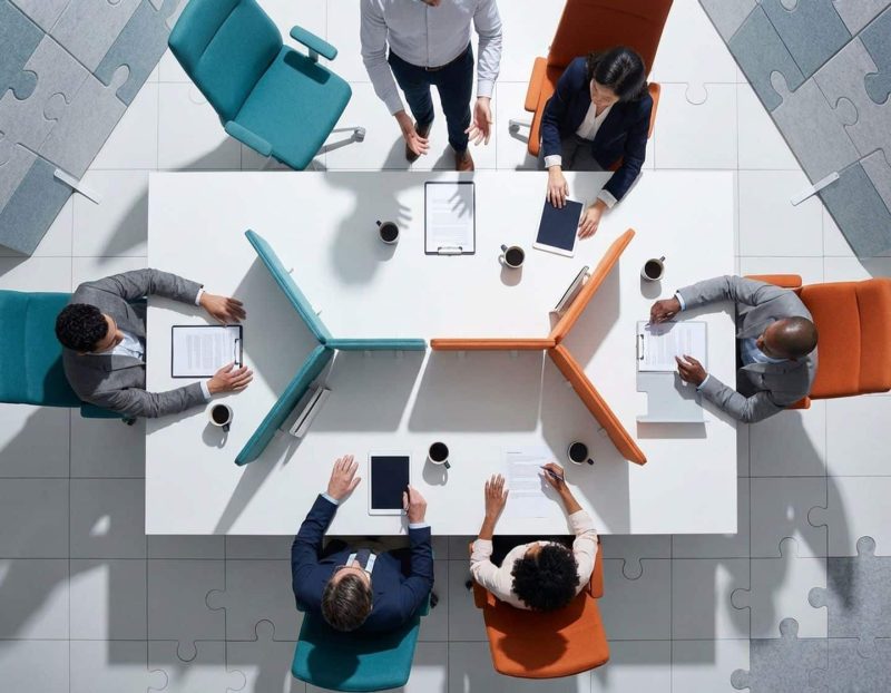 diverse professionals werken samen rond witte vergadertafel vanuit vogelperspectief met moderne kantoorinrichting