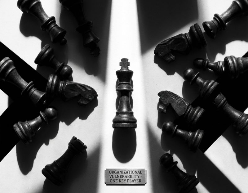 houten schaakkoning staat rechtop omringd door gevallen stukken in zwart-wit dramatische belichting op witte ondergrond