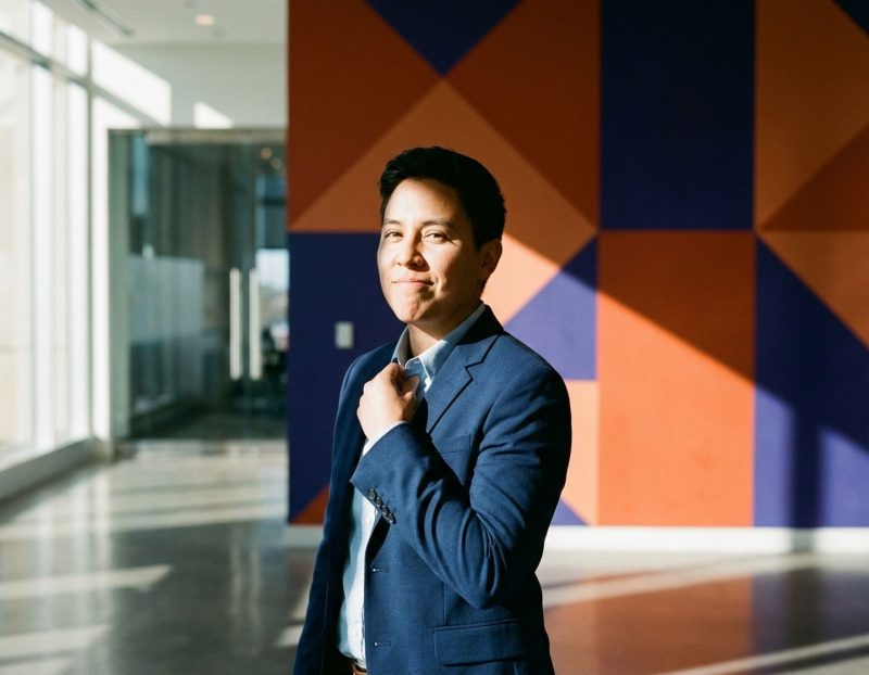 zelfverzekerde tech professional in marineblauw jasje tegen geometrische oranje en blauwe muur met dramatische belichting