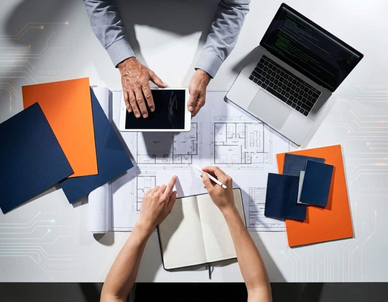 diverse handen van verschillende leeftijden werken samen aan technische blauwdrukken en digitale apparaten op wit oppervlak