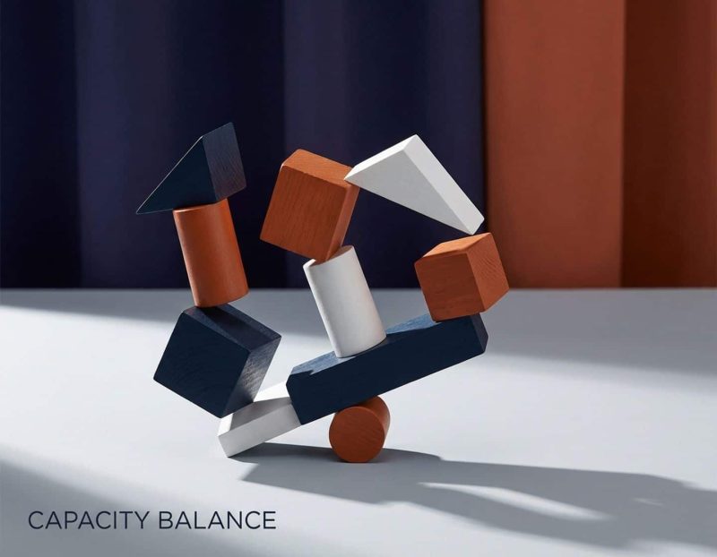 geometrische houten blokken in marineblauw, oranje en wit gestapeld in dynamische balans tegen minimalistische achtergrond.